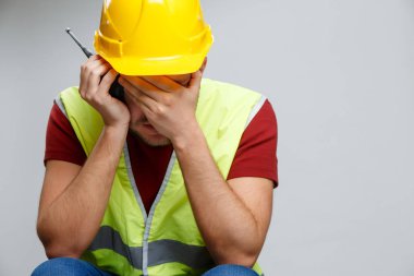 Photo of unhappy builder man in yellow helmet with walkie-talkie.