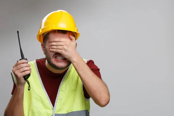 Afbeelding van verstoord Builder man in gele helm met walkie-talkie op lege grijze achtergrond. — Stockfoto