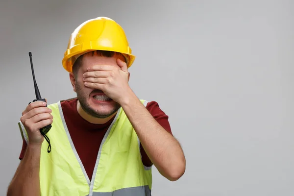 Imagen del constructor trastornado en casco amarillo con walkie-talkie sobre fondo gris vacío . — Foto de Stock