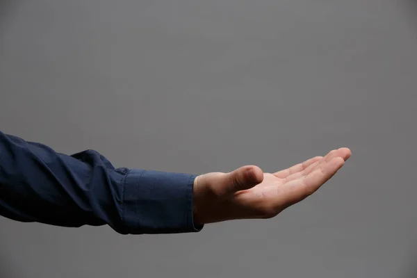 Foto der ausgestreckten Hand im blauen Hemd, Handfläche nach oben auf leerem grauen Hintergrund. — Stockfoto