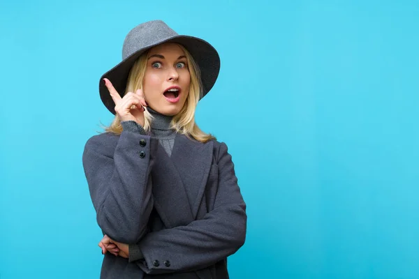 Фото счастливой блондинки в шляпе, указывающей пальцем вверх — стоковое фото