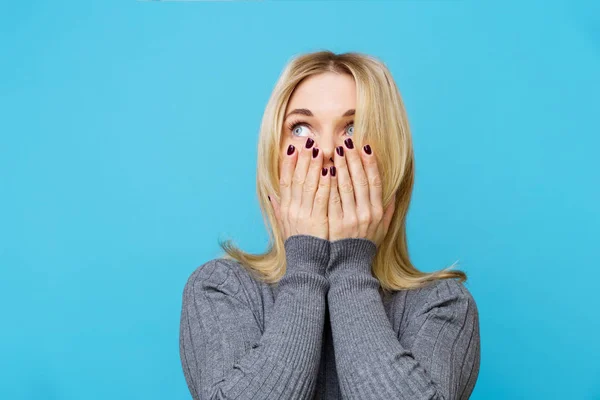 Fotografie blondýny zakrývající její ústa dlaněmi na prázdné modré pozadí — Stock fotografie