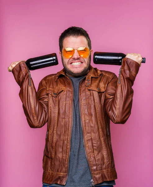 Foto do homem morena sorridente em óculos de laranja e jaqueta de couro com duas garrafas nas mãos — Fotografia de Stock