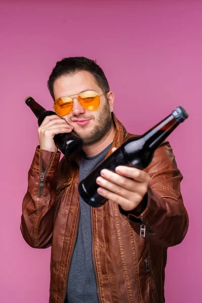 Foto de hombre moreno en gafas naranjas y chaqueta de cuero con dos botellas en las manos — Foto de Stock