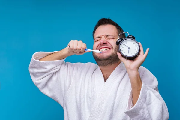 Foto van de mens met gesloten ogen met tandenborstel en wekker in handen en in witte vacht — Stockfoto