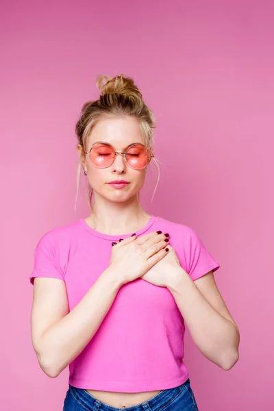 Фото блондинки в розовой футболке, держащей руки над сердцем — стоковое фото