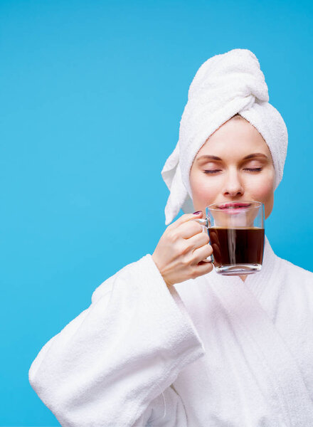 Photo of young woman in white coat and towel on her head with mug of coffee