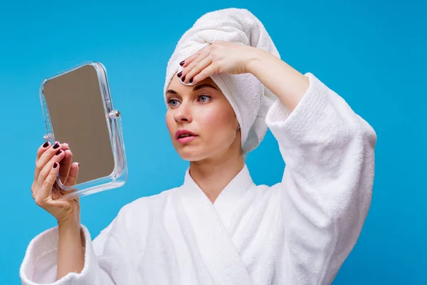 Foto van meisje in witte vacht en handdoek op haar hoofd met wattenschijfje en spiegel in haar hand — Stockfoto