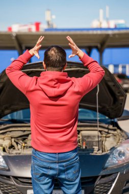 Gündüz dışarıda kırık arabanın açık kaputunun yanındaki brunet adamının sırtındaki görüntü