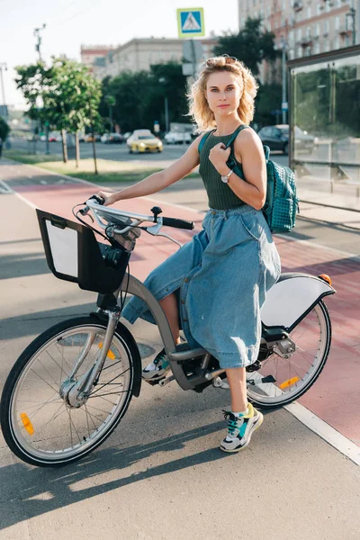 Zdjęcie młodej dziewczyny siedzącej na rowerze w pobliżu przystanku autobusowego — Zdjęcie stockowe