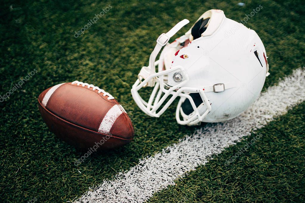 Photo of white helmet of Amerinian football player and ball on green lawn