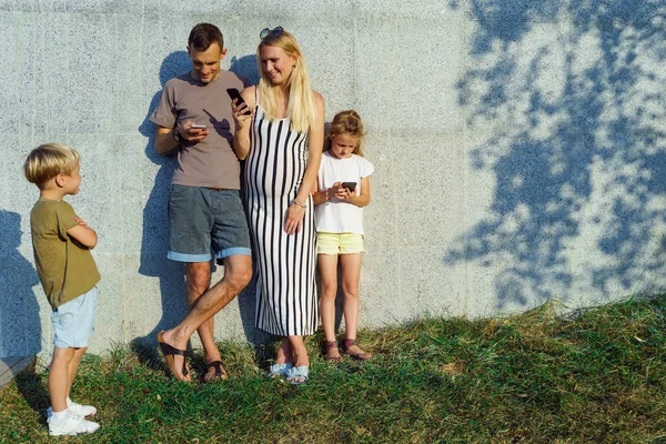 Picture of woman, man and daughter with telephones in their hands and son standing next to concrete wall on street on summer day — Stock Photo, Image