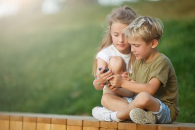 Açık havada ahşap çit üzerinde oturan telefon elleri ile küçük erkek ve kız Fotoğrafı