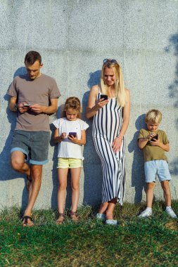 Sokakta beton duvar üzerinde duran ellerinde telefon ile sarışın kadın ve erkek ve çocukların fotoğrafları