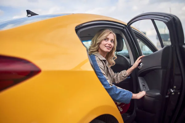 Foto de rubia sentada en el asiento trasero de taxi amarillo con puerta abierta —  Fotos de Stock