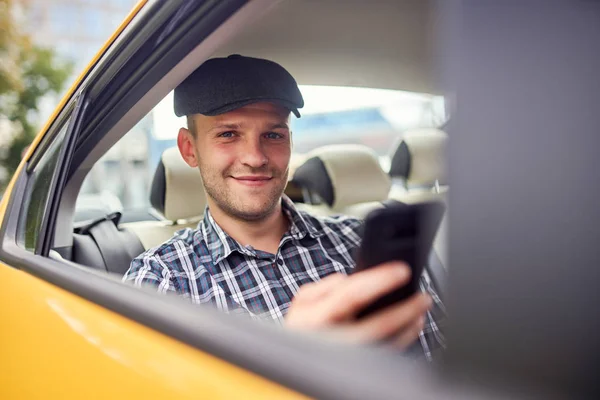 Imagen del joven en gorra con teléfono en la mano sentado en el asiento trasero en coche amarillo —  Fotos de Stock