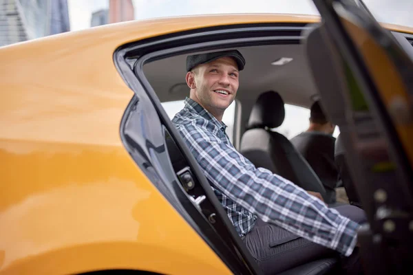 노란색 택시뒷좌석에 앉아 모자와 격자 무늬 셔츠에 젊은 남자의 이미지 — 스톡 사진