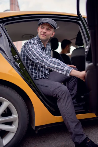 노란색 택시뒷좌석에 앉아 옆을 바라보는 모자와 격자 무늬 셔츠를 입은 청년의 이미지 — 스톡 사진
