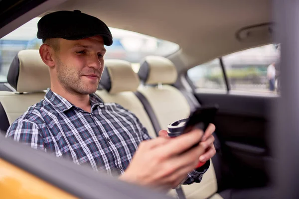 Foto de hombre con teléfono y vaso de café sentado en el asiento trasero en taxi —  Fotos de Stock