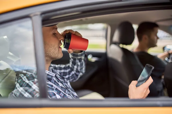 Foto de hombre con teléfono y vaso de café sentado en el asiento trasero en taxi —  Fotos de Stock