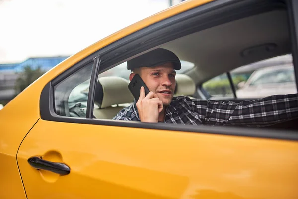 노란색 자동차의 뒷좌석에 앉아 손에 전화와 모자에 남자의 이미지 — 스톡 사진