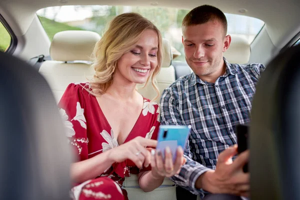 Фото счастливых женщин и мужчин с телефоном в руках, сидящих на заднем сидении автомобиля . — стоковое фото