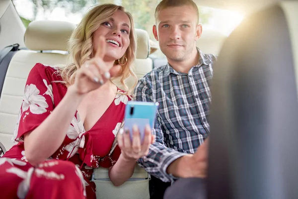 Фото счастливых женщин и мужчин с телефоном в руках, сидящих на заднем сидении автомобиля в течение дня — стоковое фото