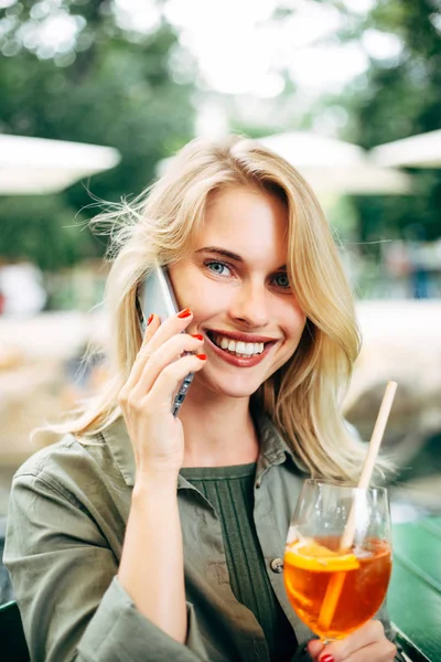 Foto einer glücklichen Blondine mit einem Cocktail in der Hand, die auf der Straße telefoniert. — Stockfoto