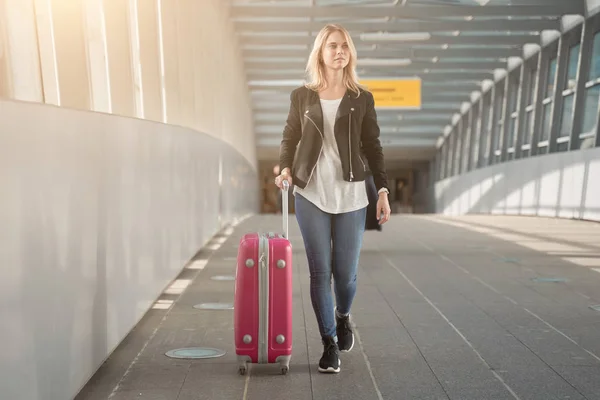 Foto de rubia con maleta rosa caminando a lo largo de la transición en el aeropuerto . — Foto de Stock