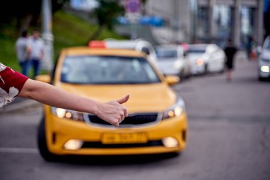 Image from back of woman with outstretched hand stopping taxi in afternoon on blurred background. clipart