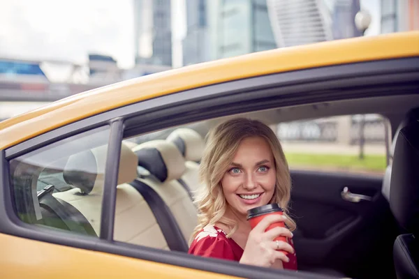 노란 택시의 뒷좌석에 앉아 그녀의 손에 커피 한 잔과 곱슬 금발의 사진. — 스톡 사진