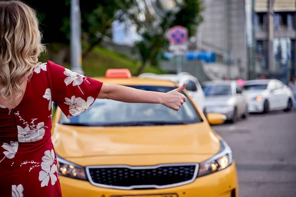 Photo from back of woman with outstretched hand stopping taxi in afternoon on blurred background . — Stock Photo, Image