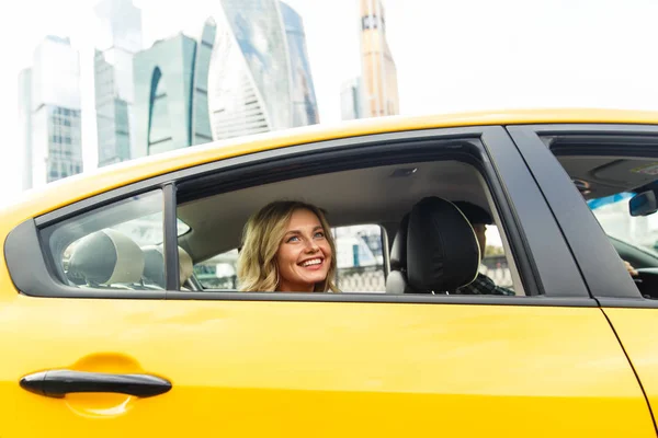 Foto de una joven sentada en el asiento trasero de un taxi amarillo en verano sobre un fondo moderno de la ciudad . —  Fotos de Stock