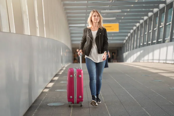 Foto de rubia con equipaje rosa caminando en el paso de peatones en el aeropuerto . — Foto de Stock