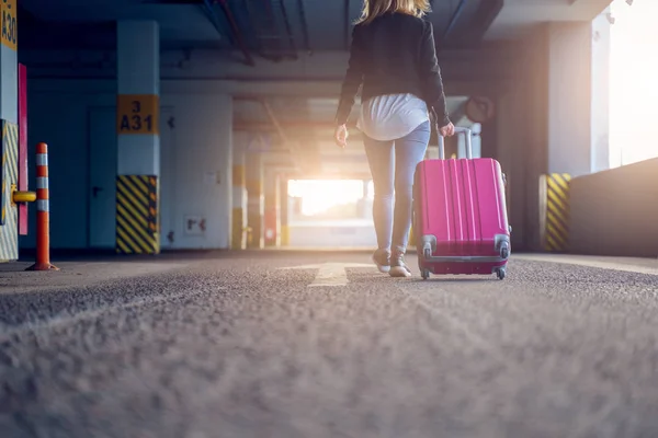 Foto de la parte posterior de la rubia con la maleta rosa caminando a lo largo del pasaje en el aeropuerto, fondo borroso — Foto de Stock