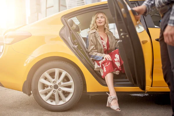 Foto di bionda in abito rosso lungo seduta in taxi e gli uomini che aprono la porta — Foto Stock