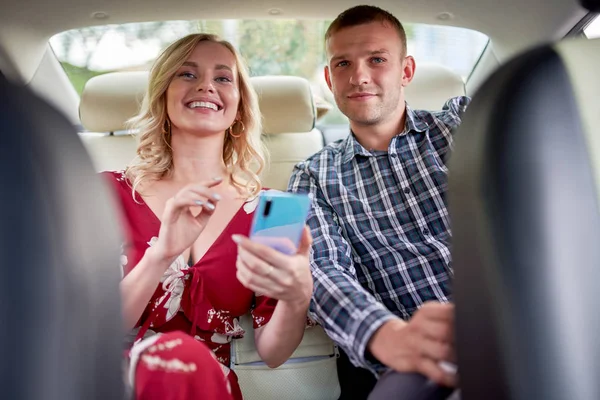 Imagen de la mujer sonriente y el hombre con el teléfono en las manos sentado en el asiento trasero del coche  . —  Fotos de Stock