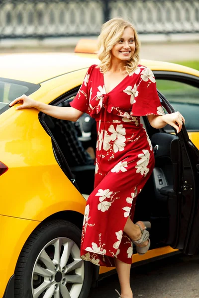 Foto de larga duración de rubia en vestido rojo parada cerca de taxi en verano . — Foto de Stock