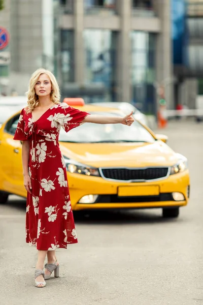Ganzkörperfoto der blonden Frau im roten Kleid, die im Sommer das Taxi stoppt. — Stockfoto