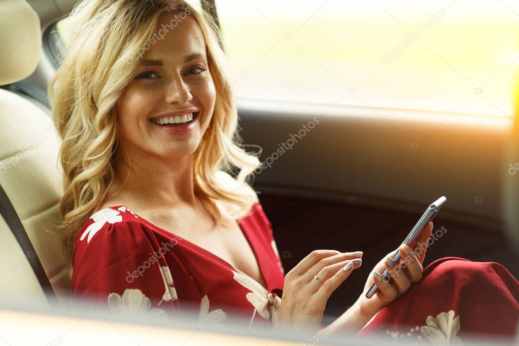 Photo of happy woman with phone in her hands sitting in back seat of car on summer.
