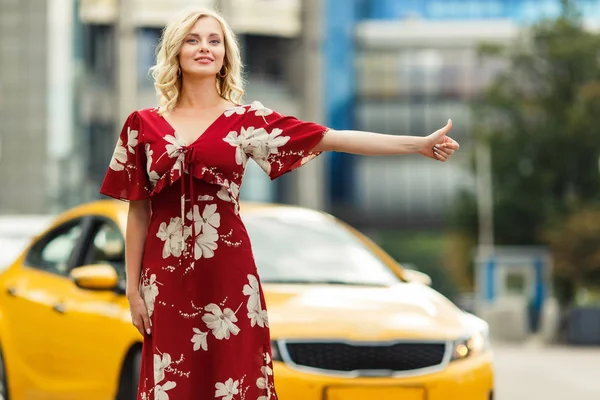Foto de loira em vestido vermelho parando táxi no verão . — Fotografia de Stock