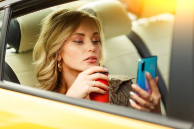 Öğleden sonra modern şehir arka plan üzerinde yaz aylarında sarı taksi arka koltukta oturan elinde kahve ve telefon ile kadın fotoğrafı