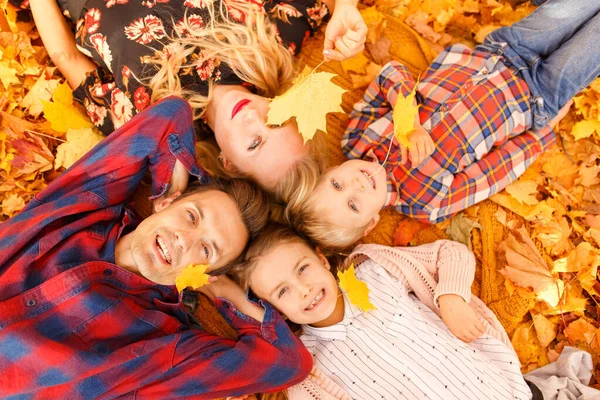 Photo from above of parents and two children lying on yellow leaves. — Stock Photo, Image