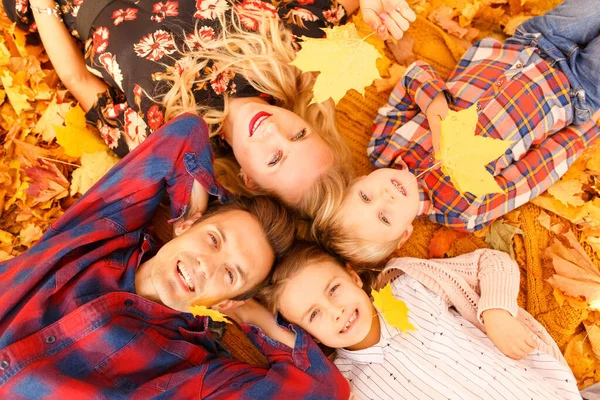 Photo from above of parents and two children lying on yellow leaves. — Stock Photo, Image