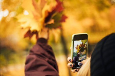 Kadınların el ele tutuşup sonbahar yapraklarını fotoğraflayan akıllı telefonları.