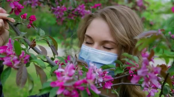 Hermosa chica en una máscara huele flores de cerezo — Vídeo de stock