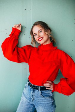 Yeşil arka planda kırmızı kazaklı mutlu sarışın.