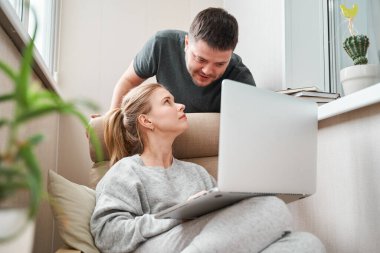 Dizüstü bilgisayarlı bej koltukta oturan bir kadın ve dairede bir erkek.