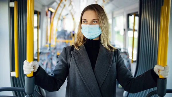 Blondýny žena v lékařské masce při pohledu na kameru, zatímco stojí v autobusovém salonku. — Stock fotografie