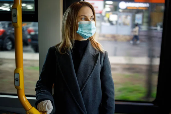 Молодая блондинка в медицинской маске держит перила, стоя в автобусной гостиной . — стоковое фото